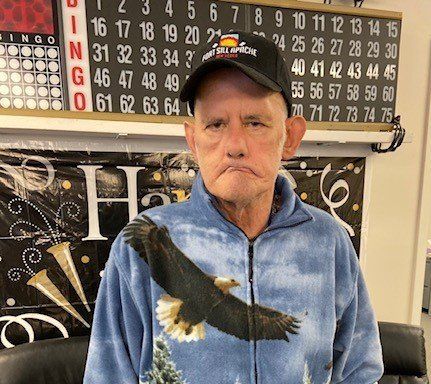 A man with an eagle on his jacket is standing in front of a bingo board.