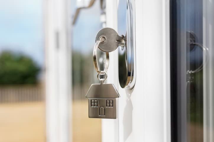 A close up of a key in a door lock with a house keychain attached to it.