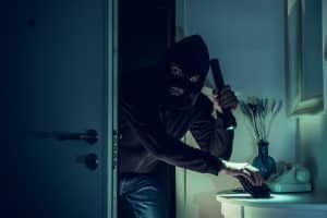 A man in a mask is breaking into a house with a hammer.