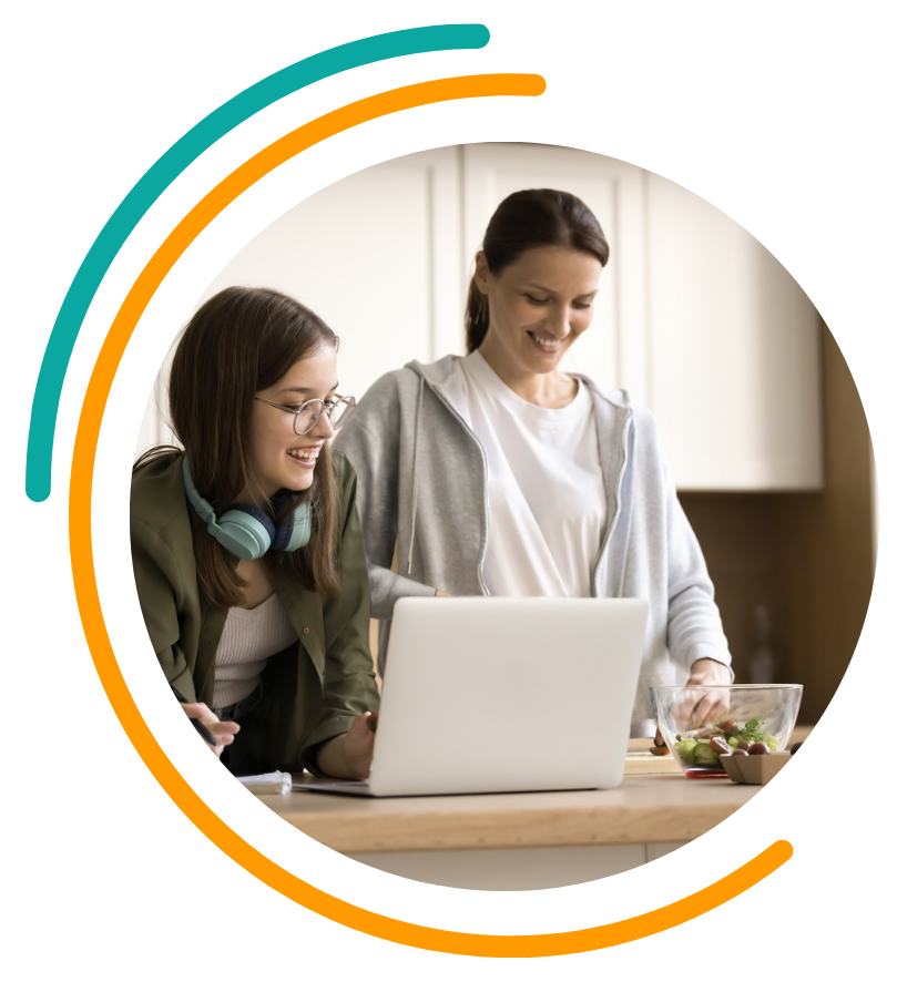 Woman and teen smiling, looking at laptop on kitchen counter. Green and orange accents.