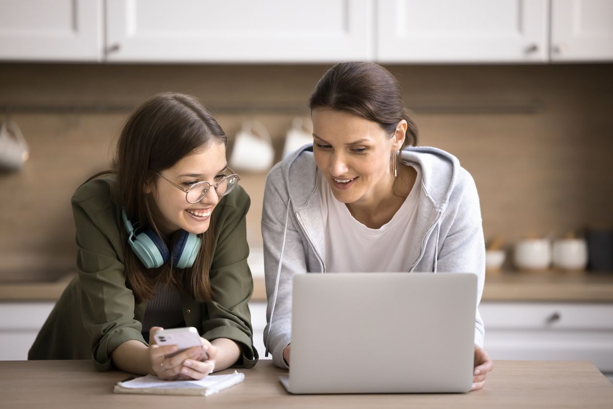 A mother and daughter are sitting at a table looking at a laptop.