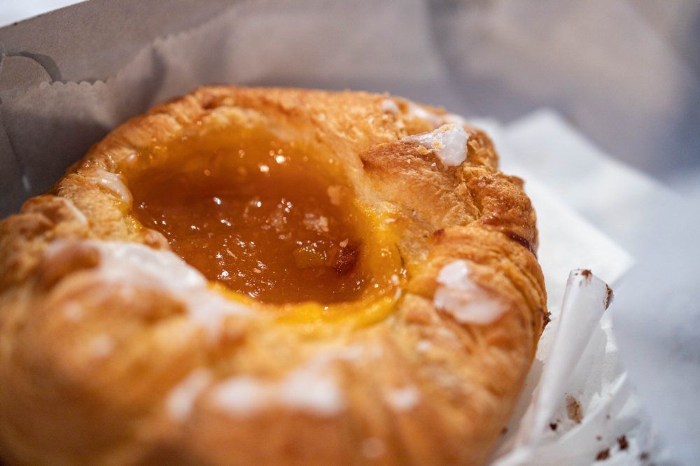 Close-up of a pastry with a golden-brown, flaky crust and a center filled with apricot jam, in a paper bag.