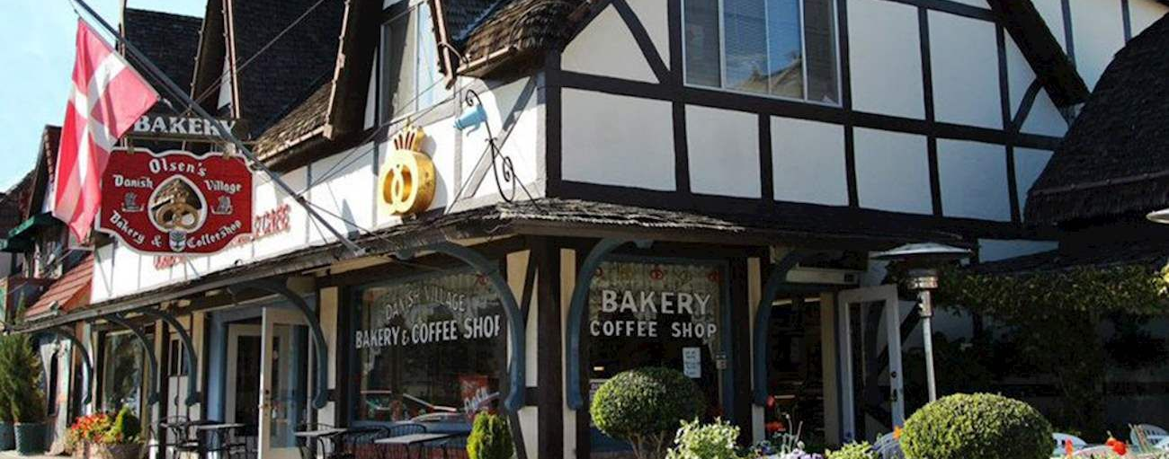 A bakery interior filled with display cases of various baked goods. A person in a red shirt is seen behind the counter.