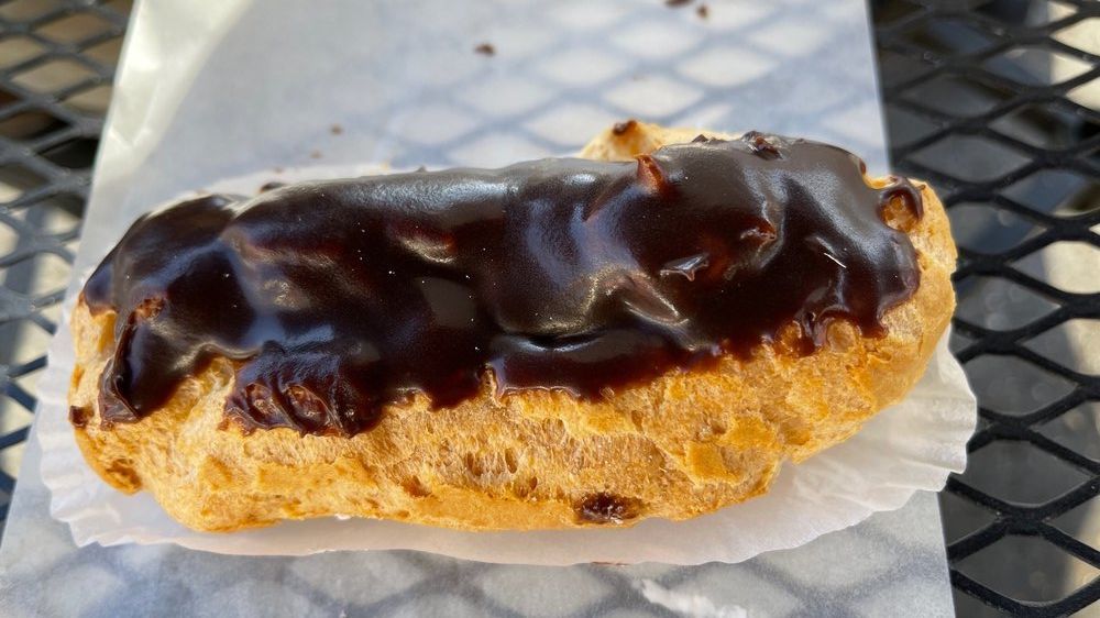 Chocolate-covered éclair on white paper, on a dark metal table.