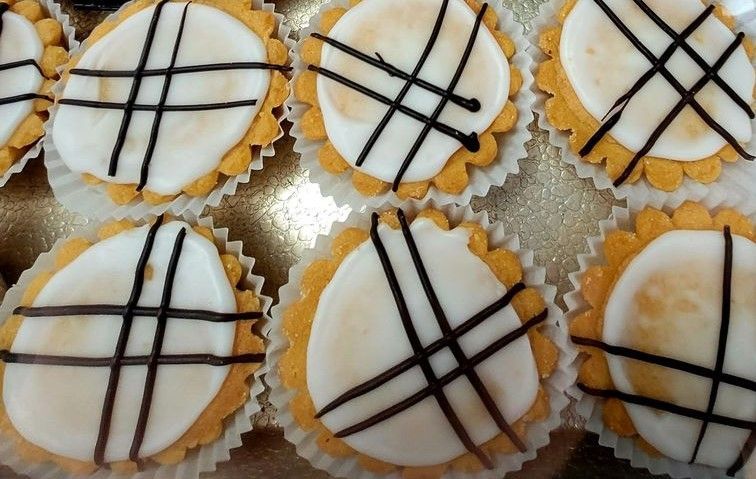 Mini tarts with white frosting and black lattice design, in paper cups.