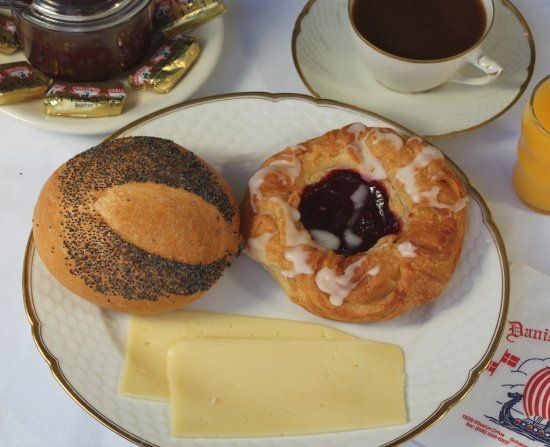 Breakfast plate with poppyseed roll, pastry with jam, cheese slices, coffee, jam, butter, and orange juice.