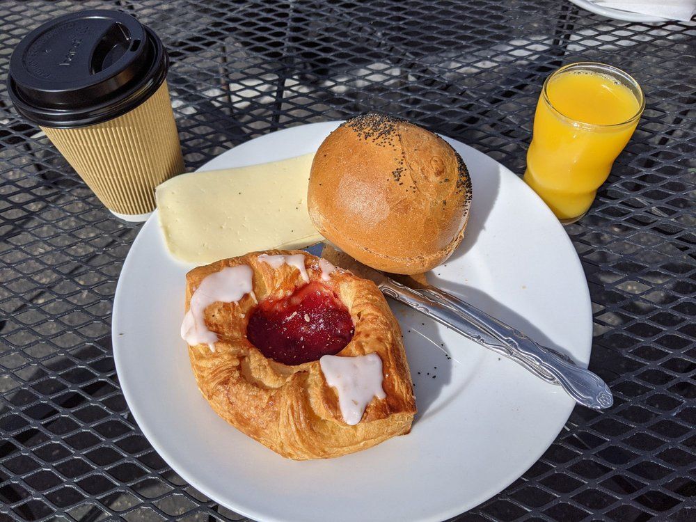 Breakfast plate with pastry, bagel, butter, coffee, and orange juice on a metal table.