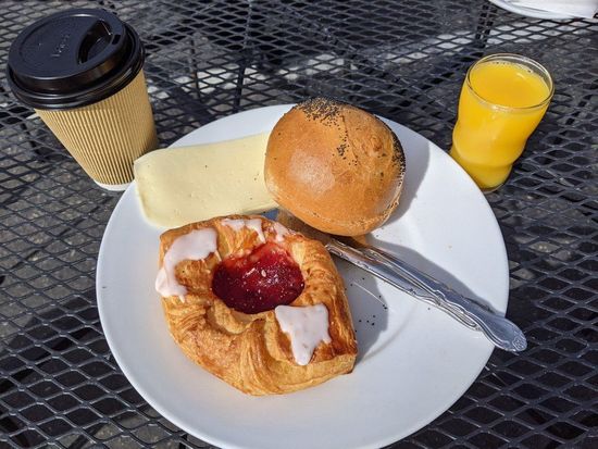 Breakfast plate with pastry, bagel, butter, coffee, and orange juice on a metal table.