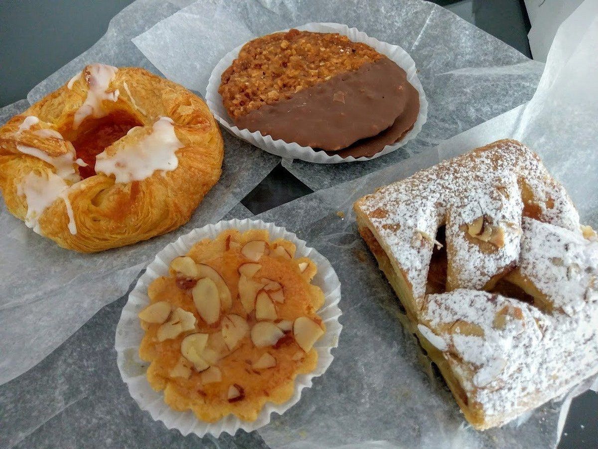 Pastries on parchment paper: danish, cookie dipped in chocolate, tart, and rectangular pastry dusted with powdered sugar.
