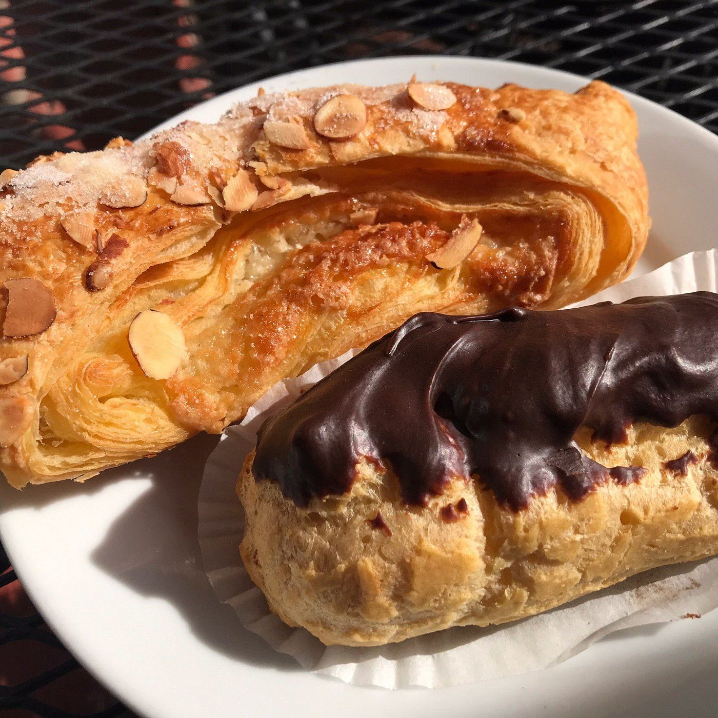 Pastry on a white plate: almond danish and chocolate éclair in sunlight.
