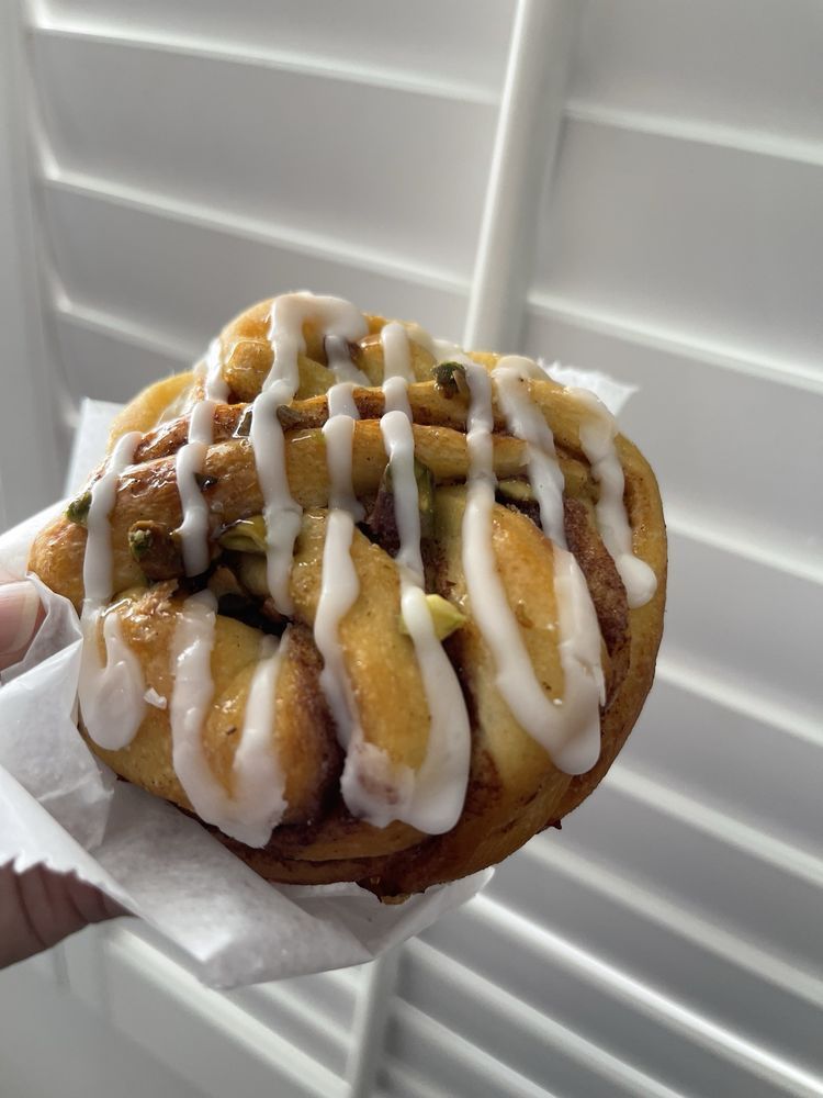 Pistachio cinnamon roll with white icing, held in hand, against a white shutter background.