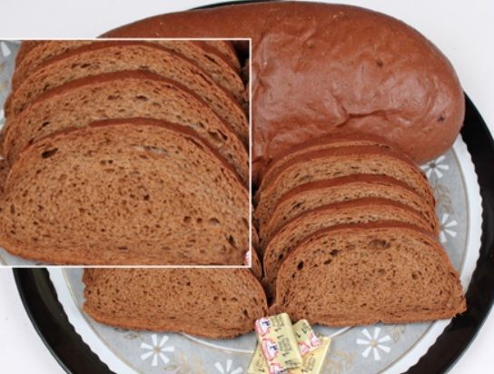 Loaf of brown bread, partially sliced, on a decorative plate, with pats of butter.