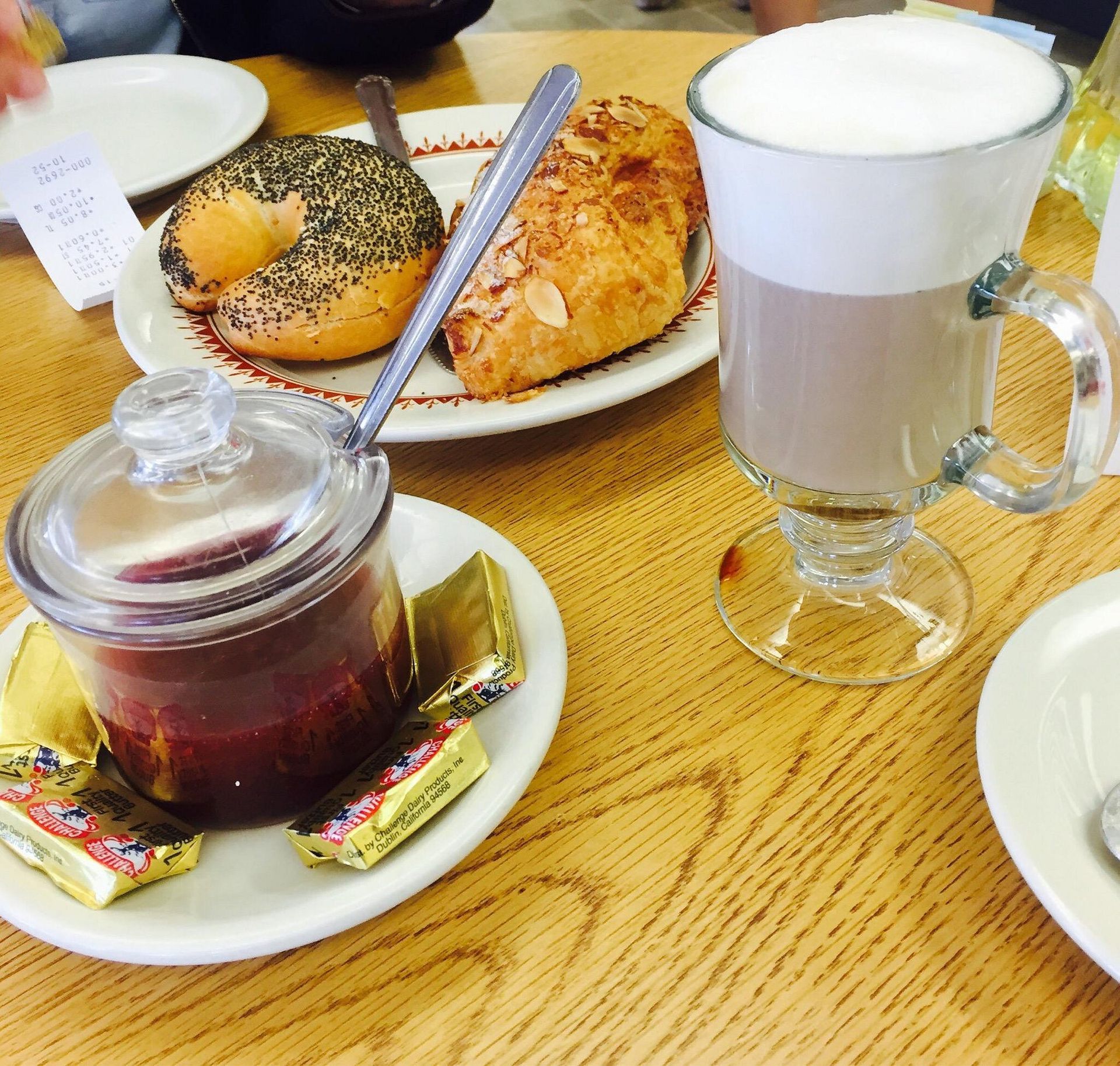 Bagel, croissant, jam, butter, and coffee on a wooden table.