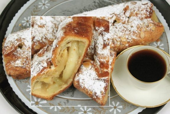 Apple pastry with powdered sugar on a plate next to a cup of coffee.