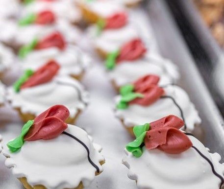 Mini pastries with white icing, red flower decorations, and green leaves on a tray.