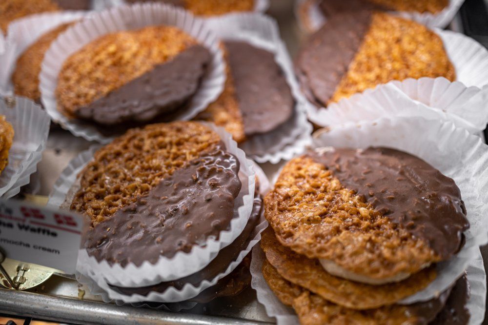 Chocolate-dipped waffle cookies in white paper cups, displayed on a surface.