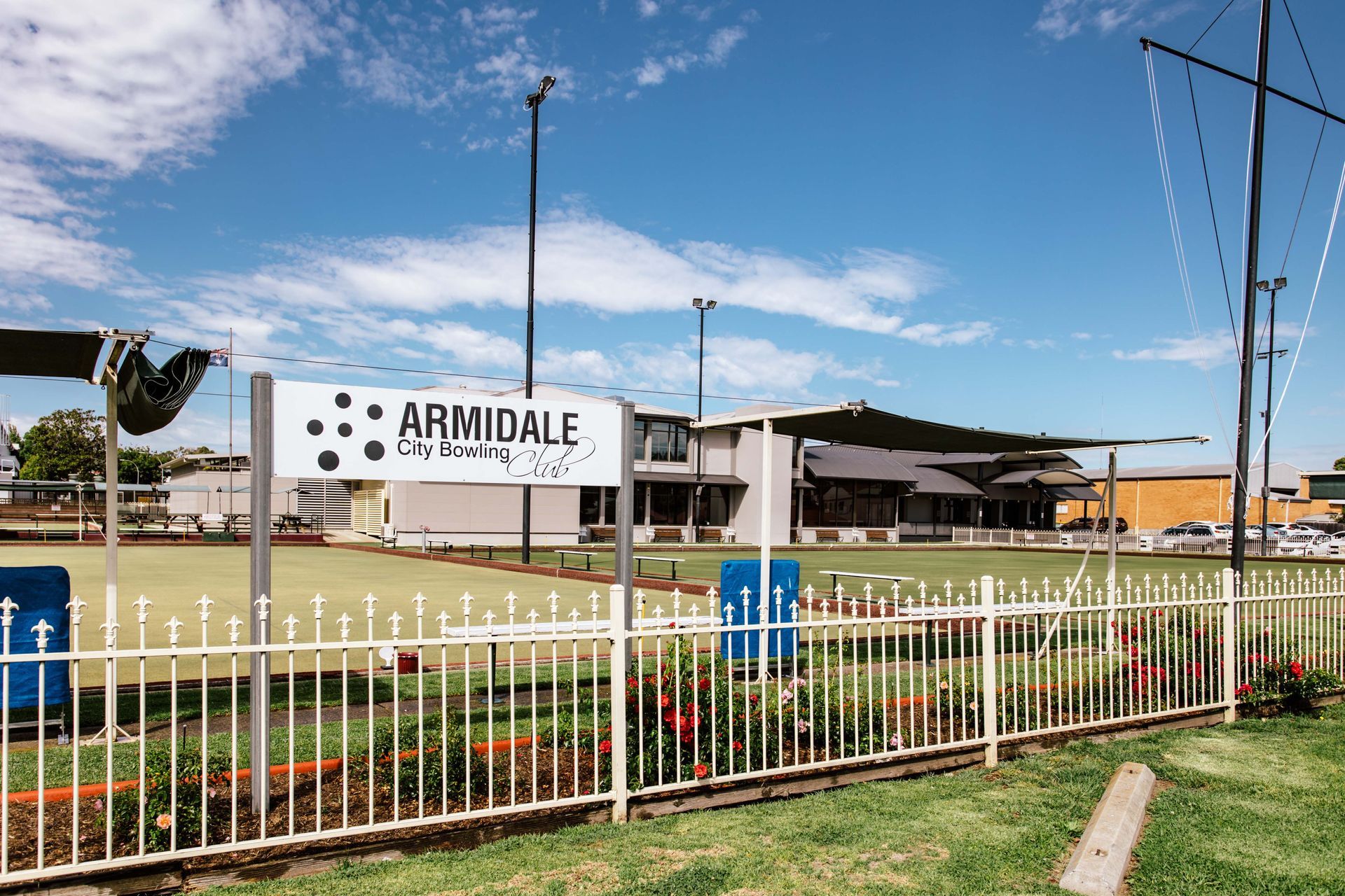 A white sign that says ' Armidale City Bowling Club ' on it stands in front of bowling greens
