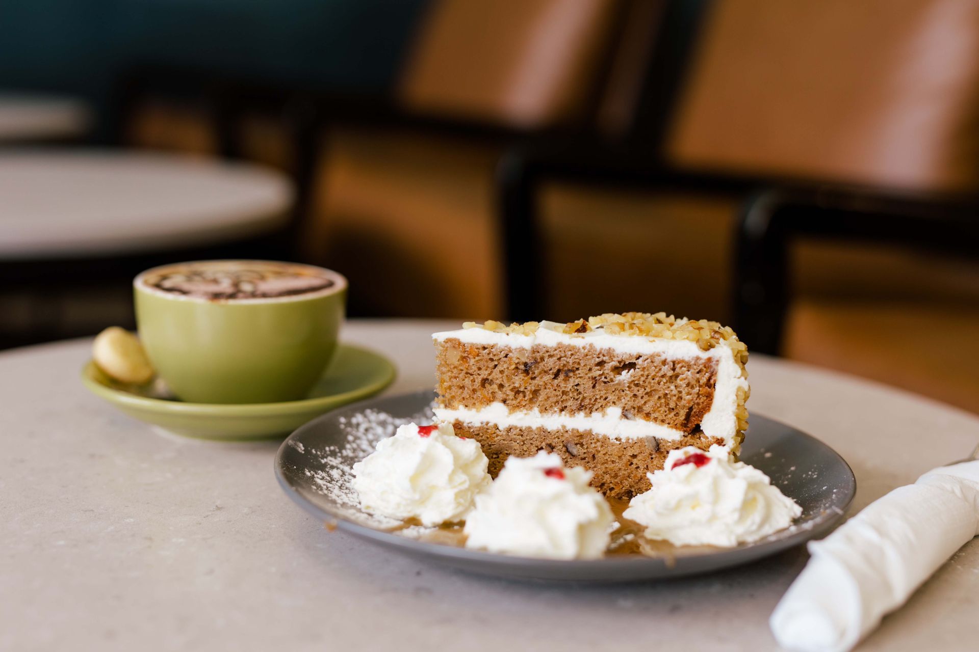 A slice of carrot cake on a plate next to a cup of coffee