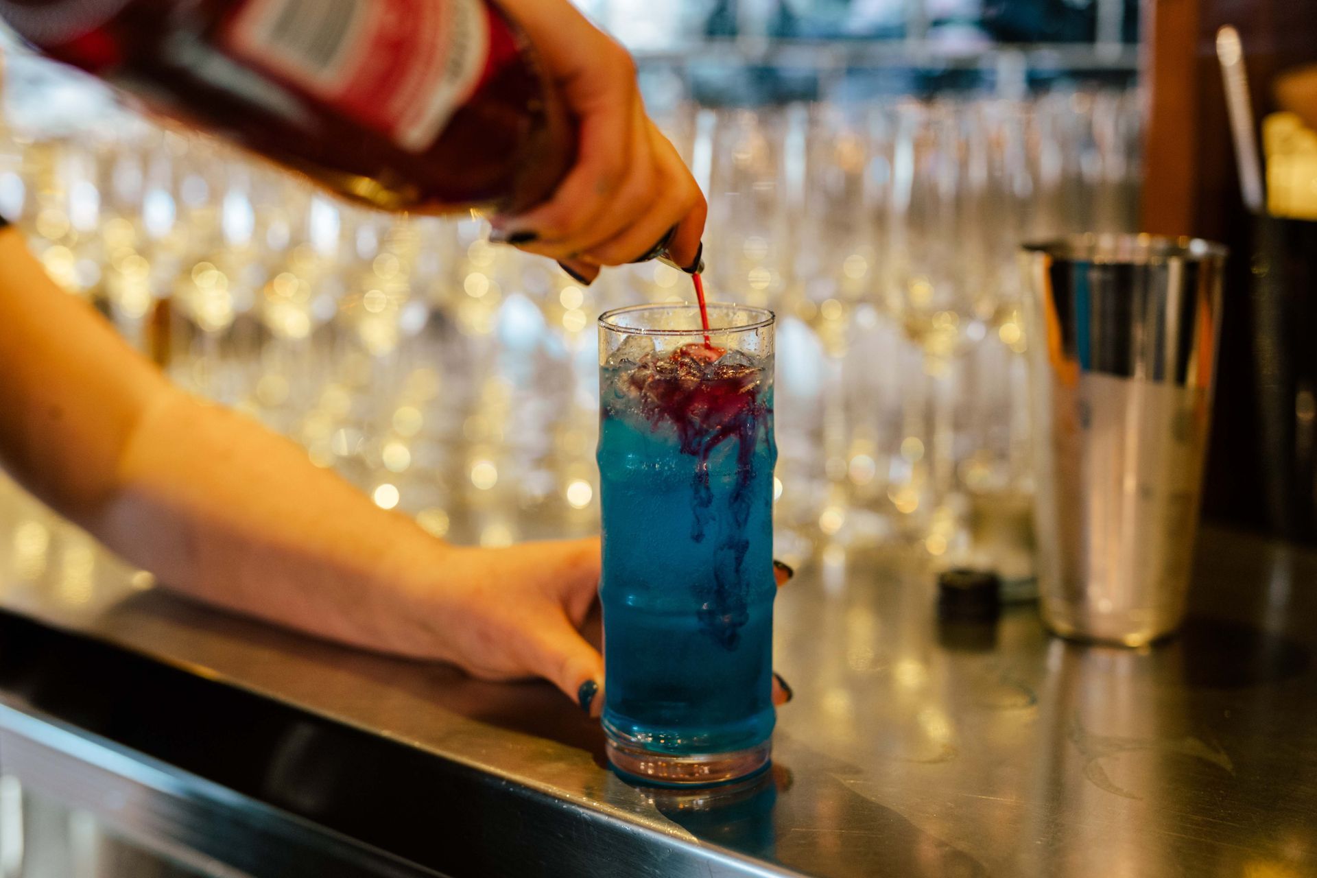 A bartender is pouring a blue drink into a glass