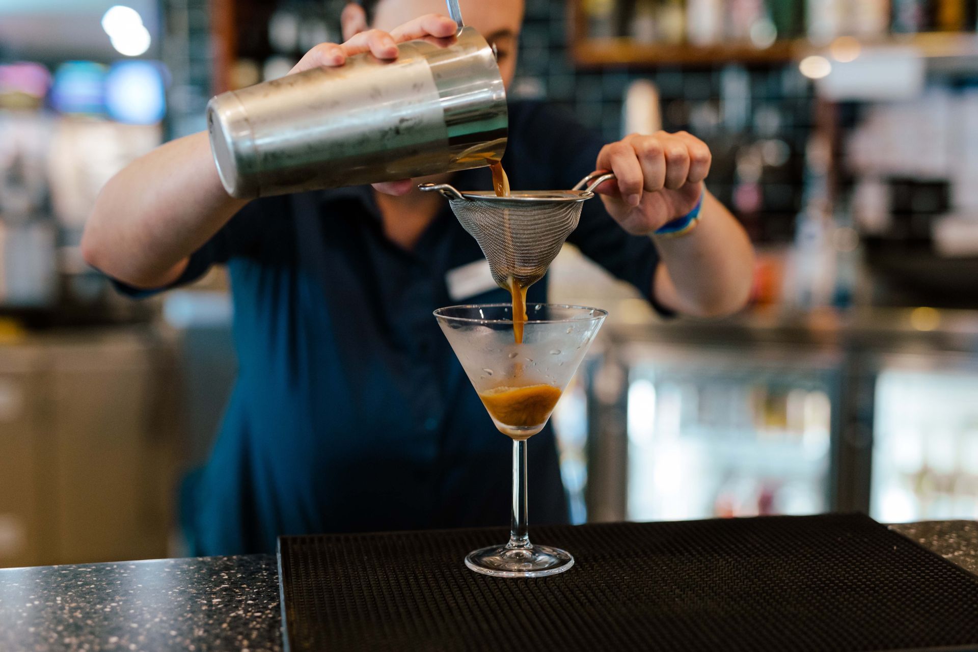 A bartender is pouring a drink into a martini glass