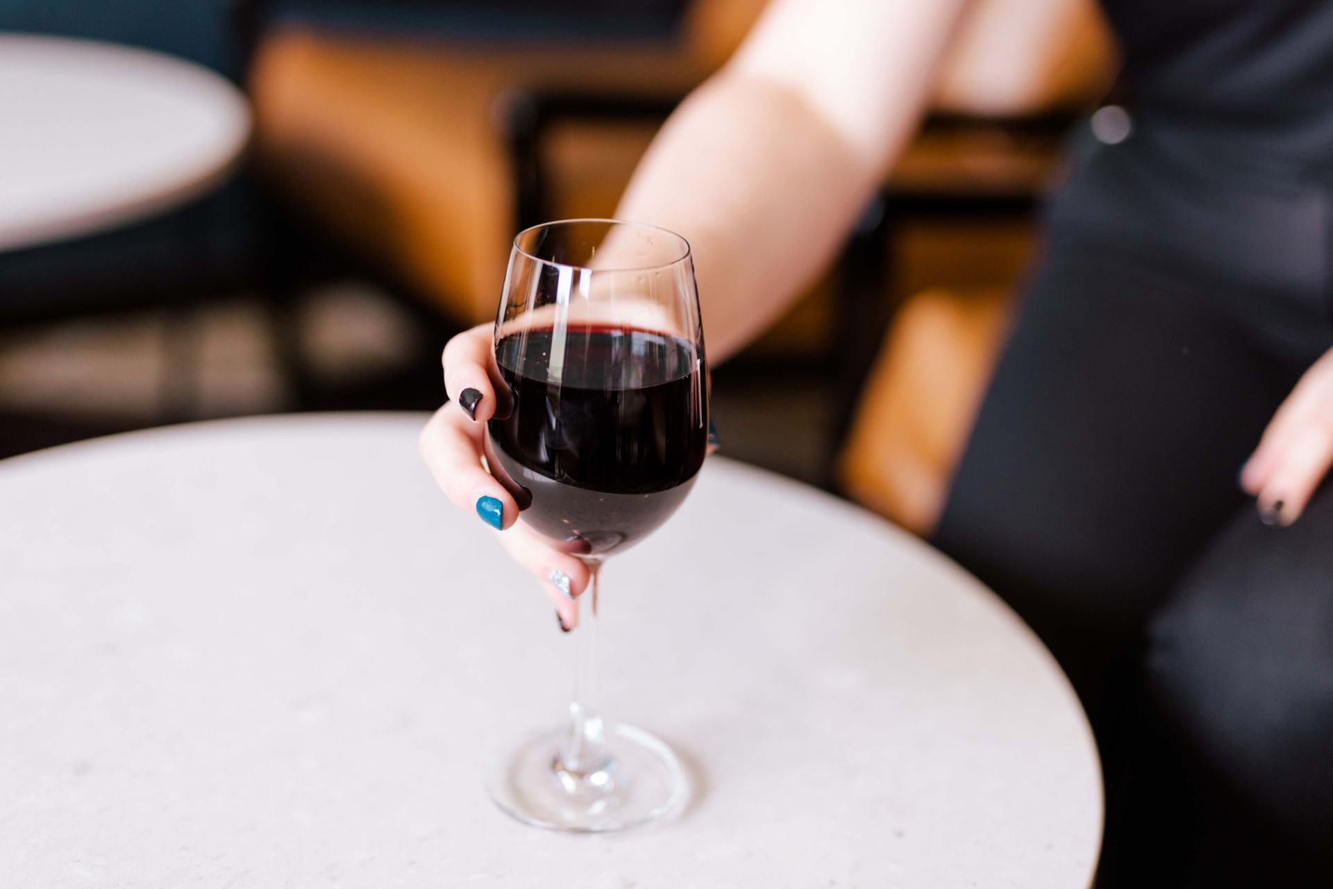 A woman is holding a glass of red wine on a table