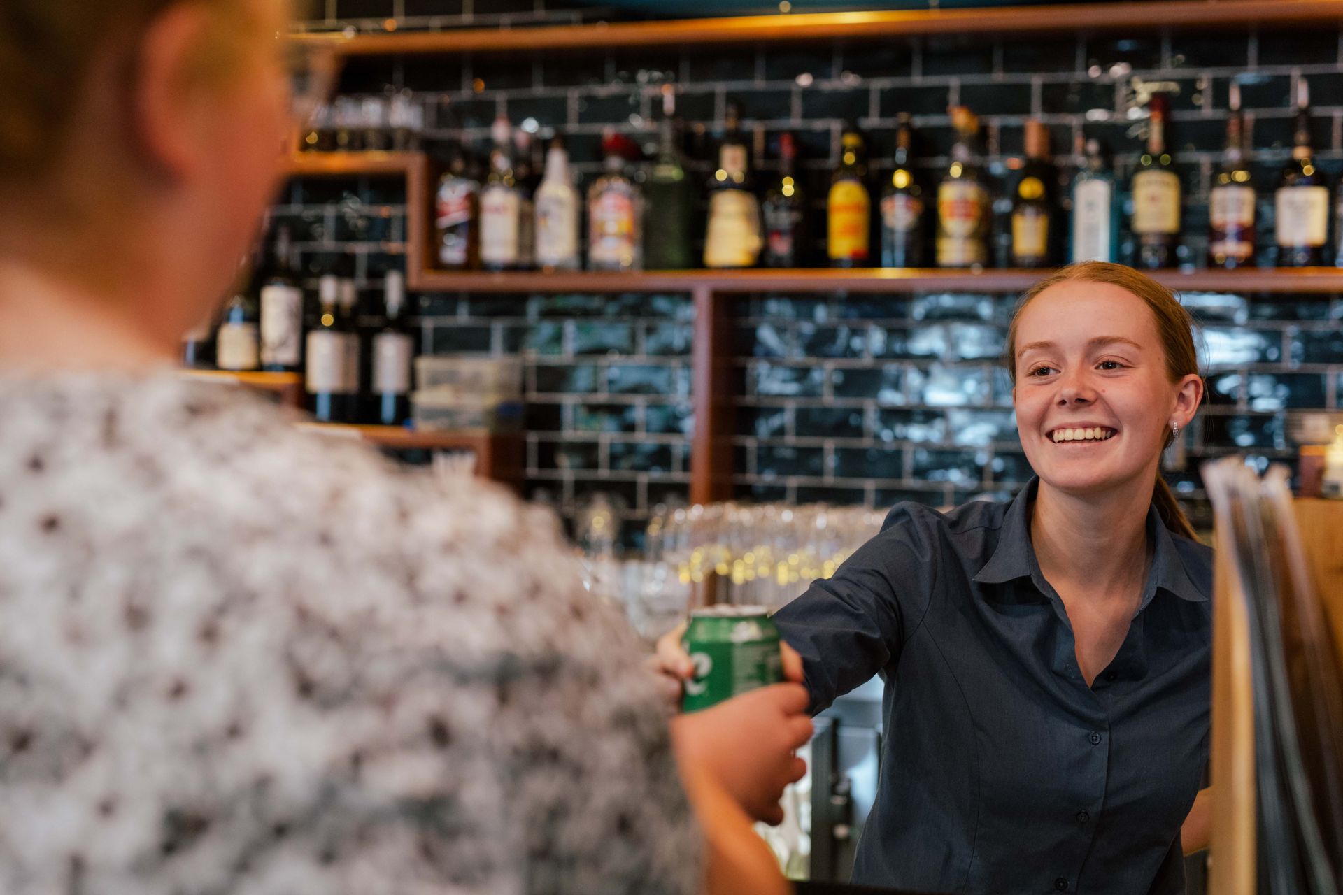 A woman is serving a drink to another woman at a bar.