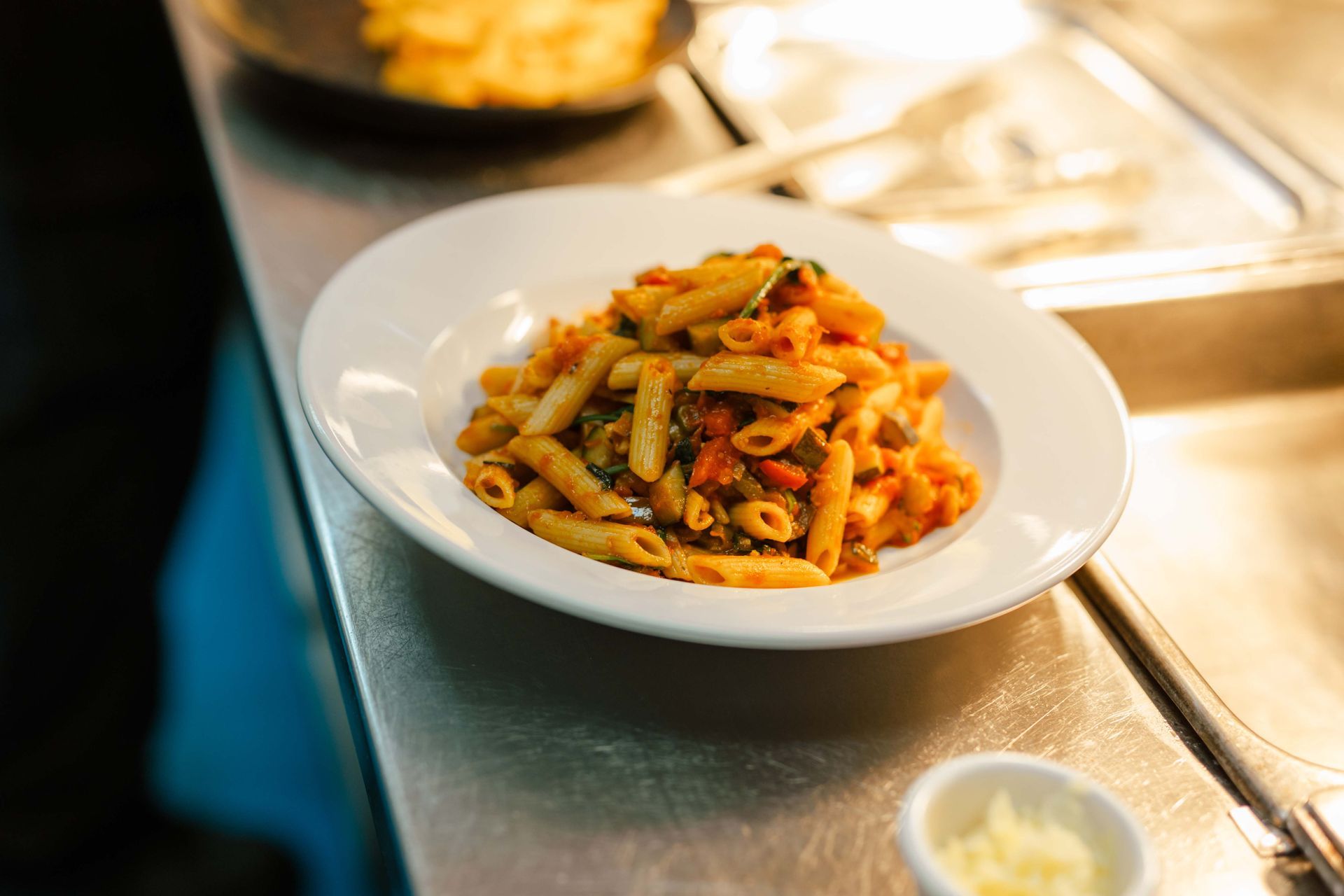 A plate of pasta sits on a counter next to a small bowl of cheese
