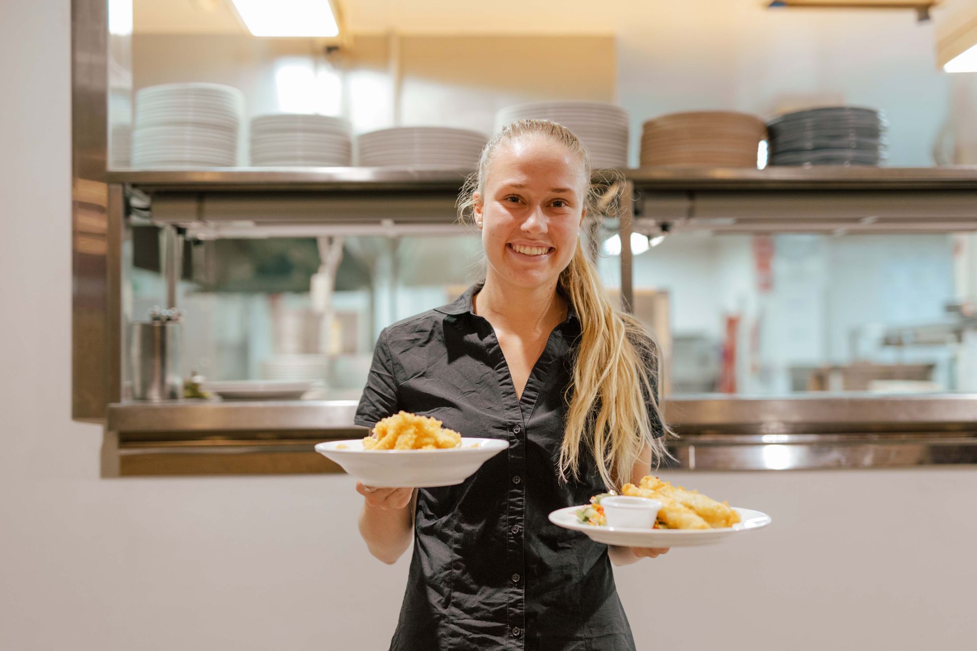 A woman in a black shirt is holding two plates of food