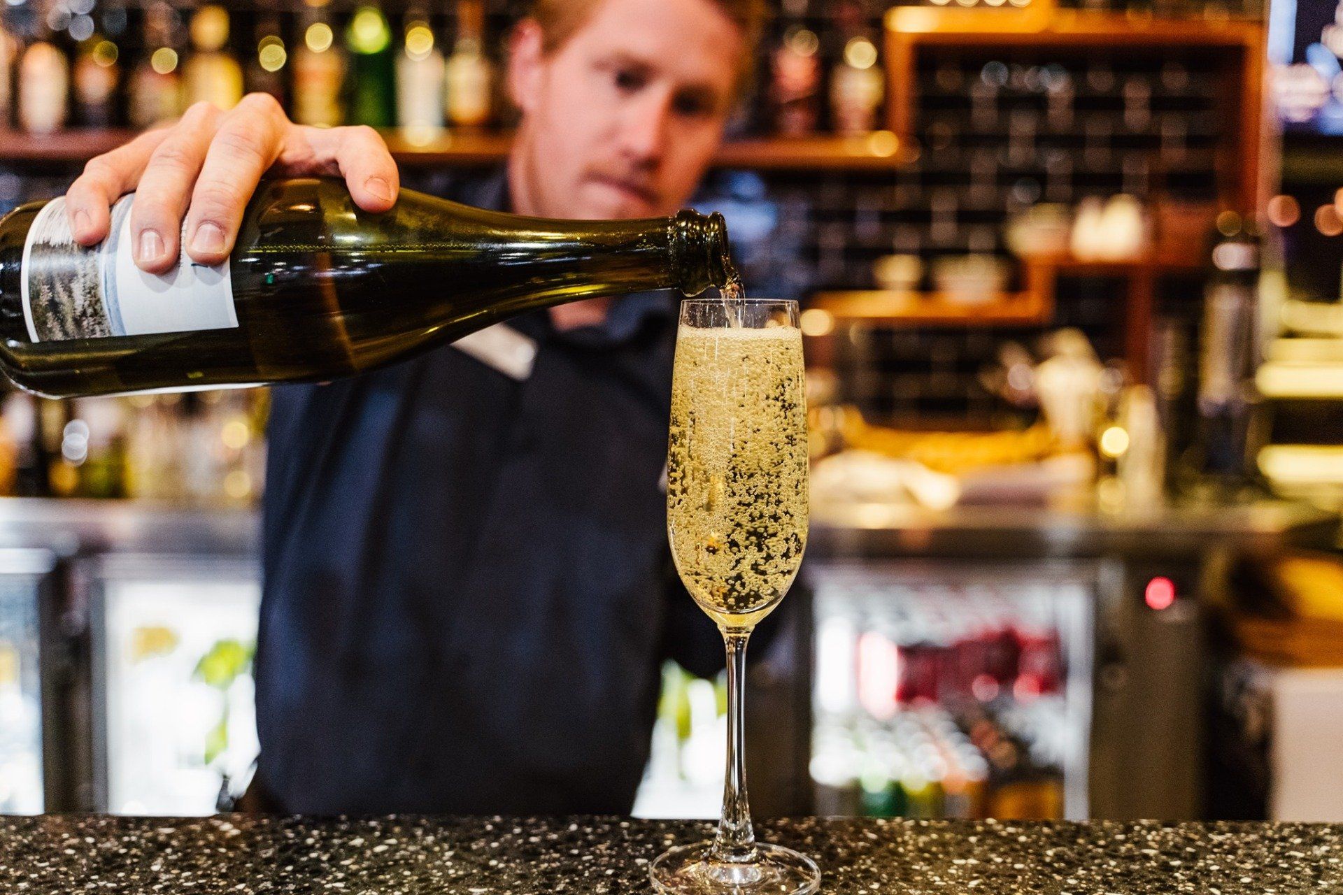 A bartender pours a glass of champagne from a bottle