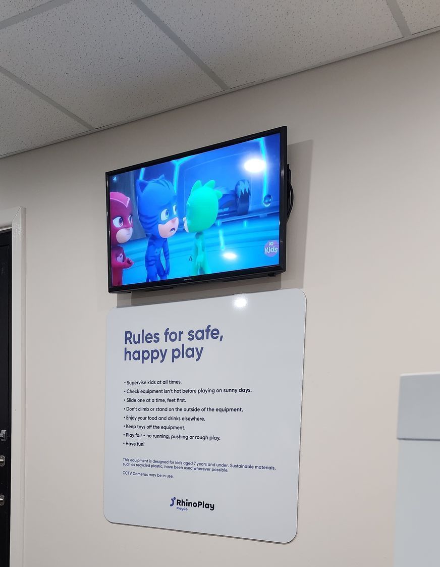 A TV above a white board with rules for safe happy play written on it