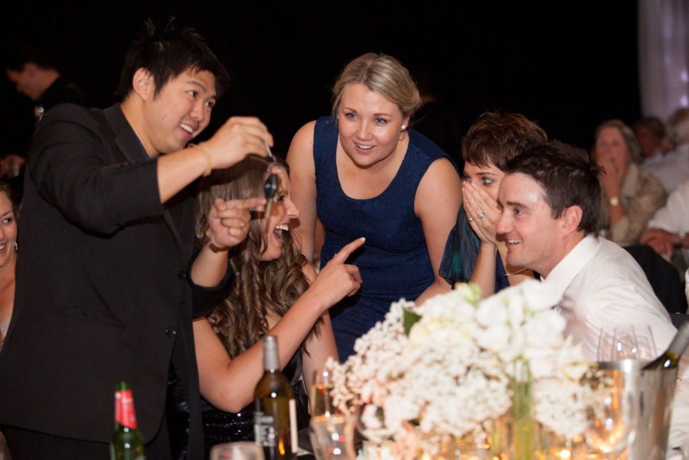 A group of people are sitting at a table watching a man perform a trick