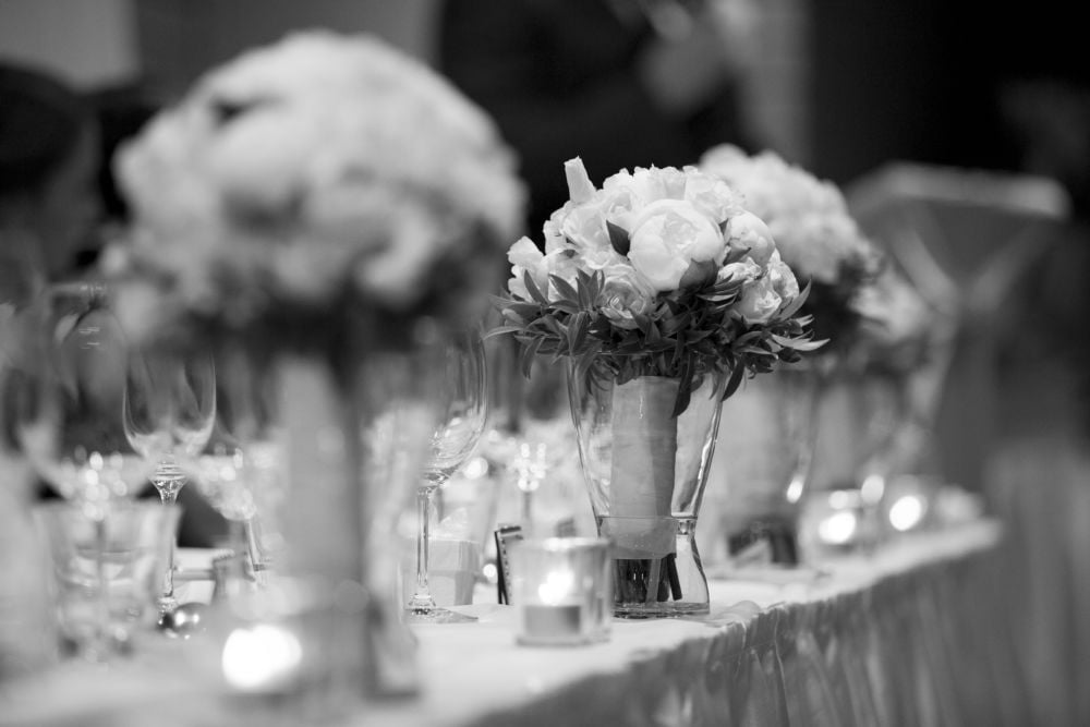 A black and white photo of a long table with flowers and candles.