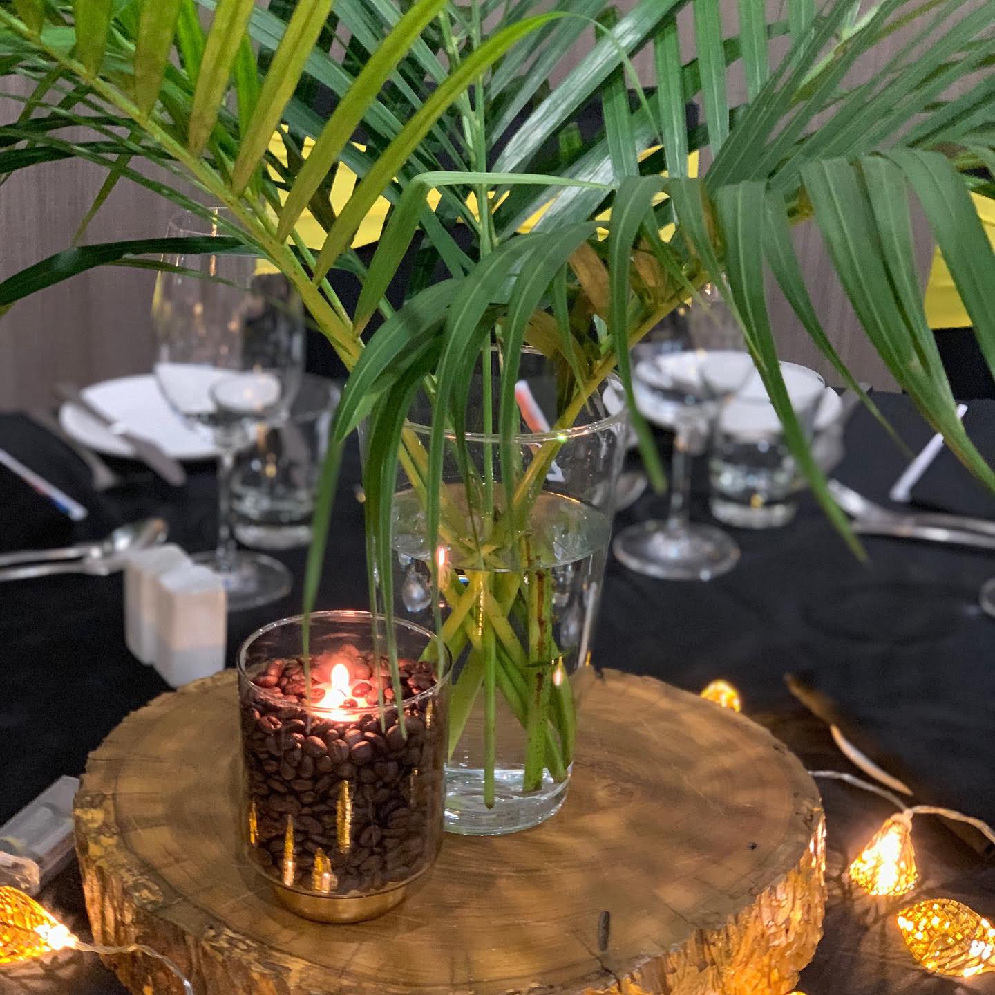 A candle sits on a wooden stump next to a vase of plants