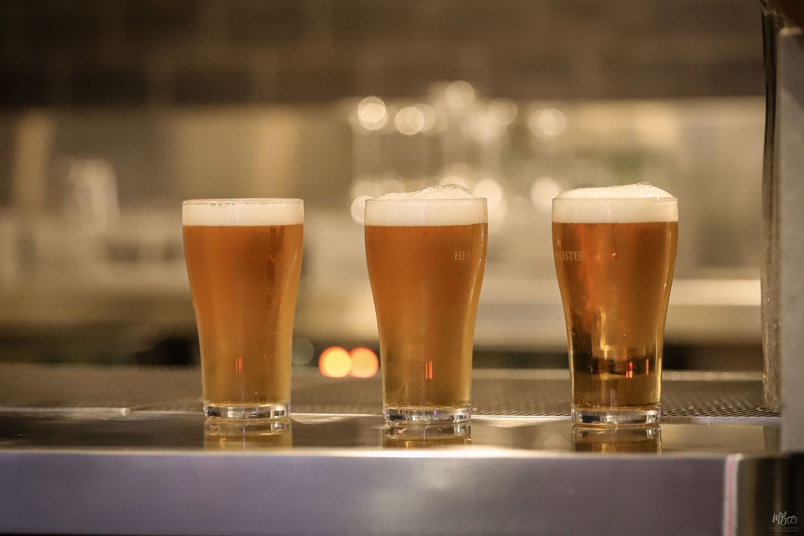 Three glasses of beer are lined up on a bar