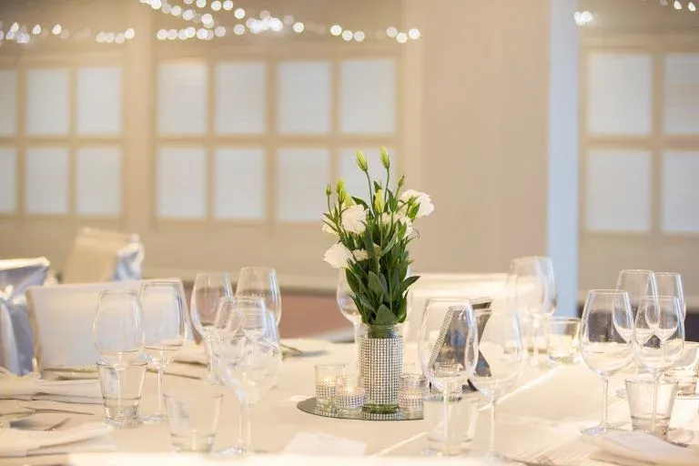 A table set for a wedding reception with a vase of flowers on it.