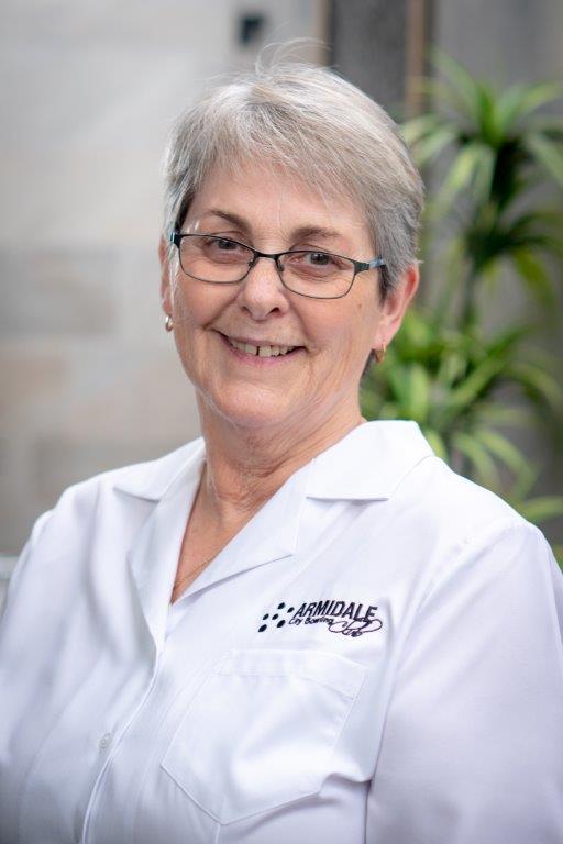 A woman wearing glasses and a white top is smiling
