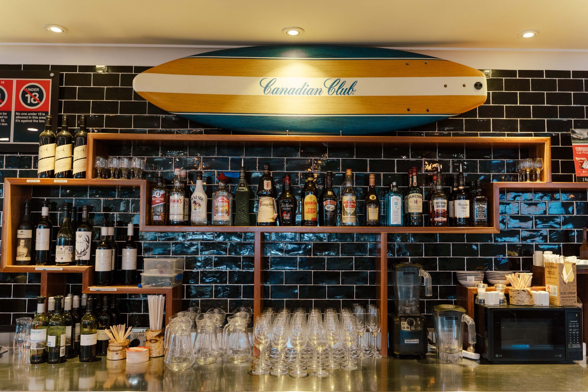 A surfboard hangs above a bar with bottles and glasses