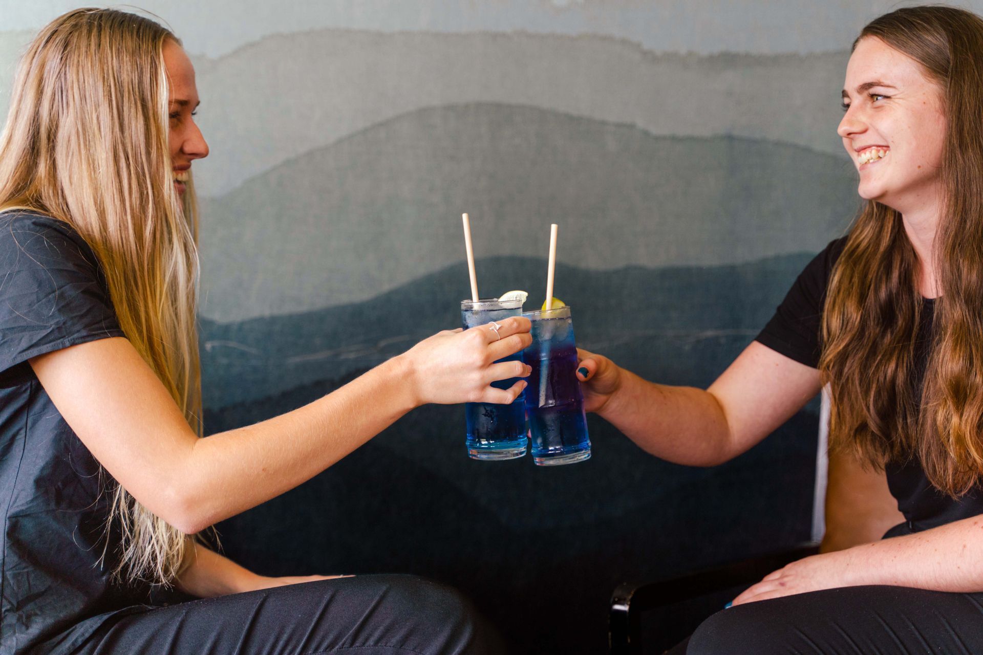 Two women toasting with blue drinks with straws