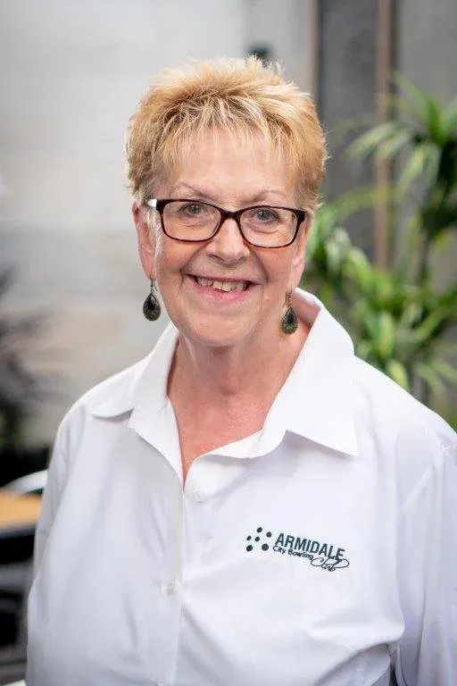 A woman wearing glasses and a white shirt is smiling