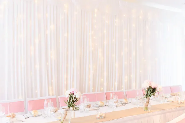A long table with flowers on it in front of a white curtain.