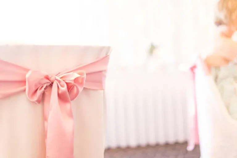 A chair with a pink bow on it is sitting in front of a table.