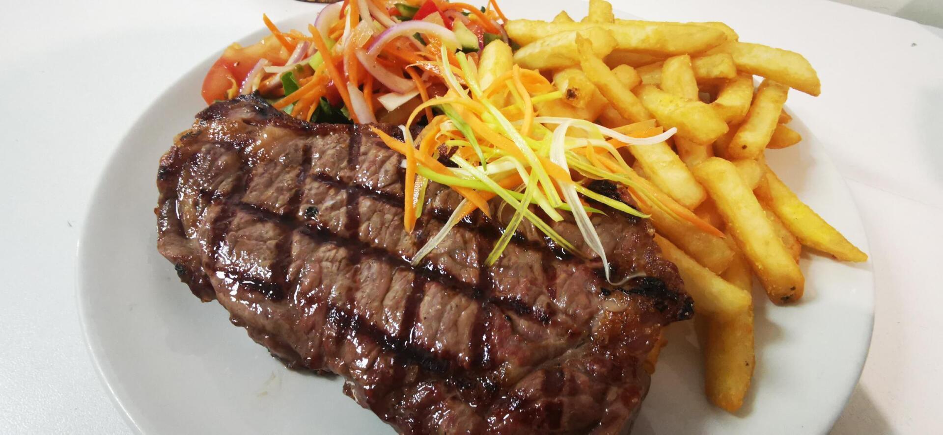 A white plate topped with a steak, salad and french fries