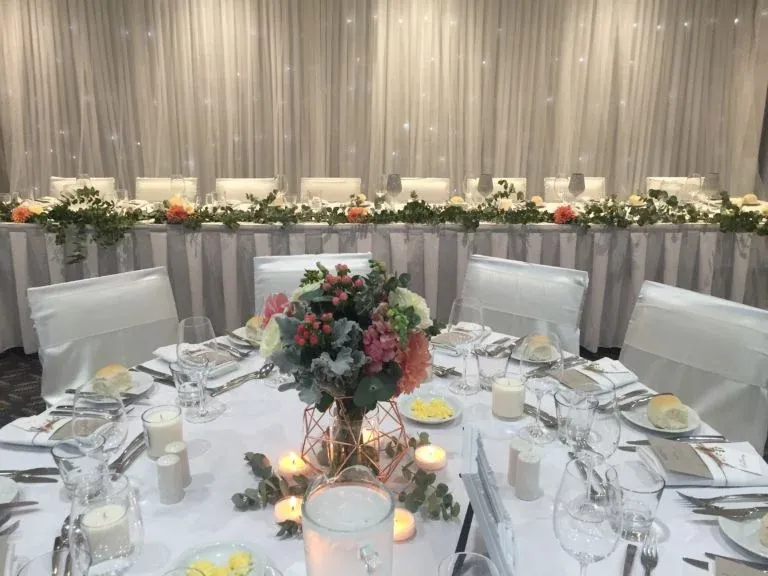 A table set for a wedding reception with a vase of flowers on it.