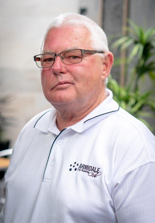 A man (Terry) wearing glasses and a white shirt is standing in front of a plant.