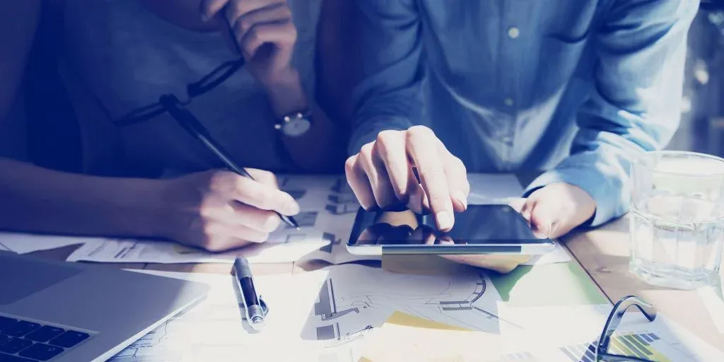A man and a woman are sitting at a table looking at a tablet.