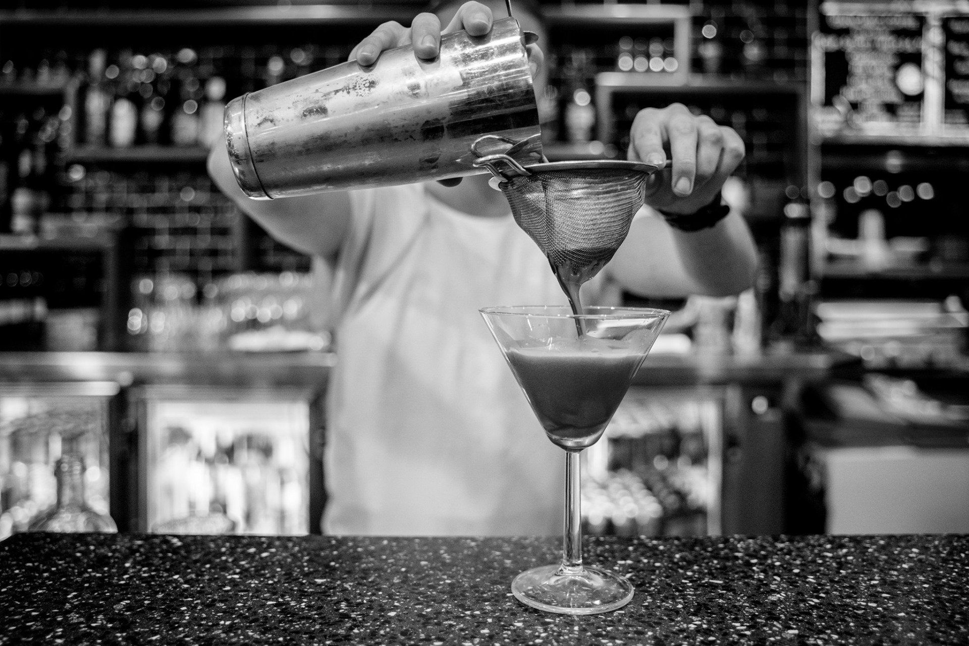 A bartender is pouring a drink into a martini glass.