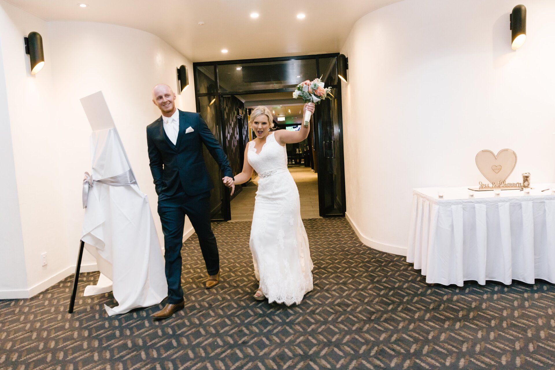 A bride and groom are walking down a hallway holding hands