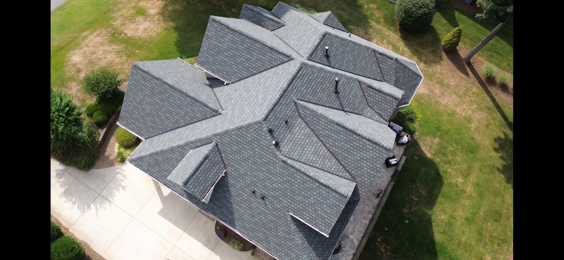 Aerial view of a house with a complex gray shingled roof and green lawn.