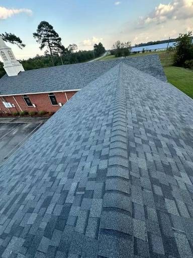 View of a building's gray asphalt shingle roof with a tree and water in the background.