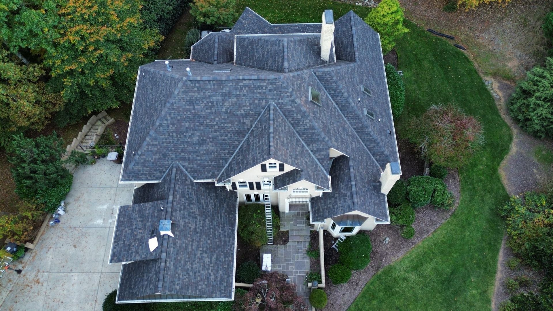 Aerial view of a large, multi-gabled house with a long driveway and surrounding trees.